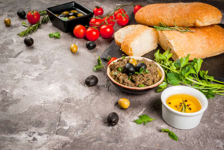 Homemade traditional Italian appetizer tapenade from green and black olives, white ciabatta, fragrant herbs and oil, fresh tomatoes. On a concrete gray table, copy spaceの写真素材