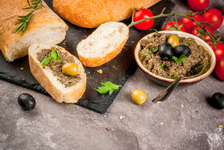 Homemade traditional Italian appetizer tapenade from green and black olives, white ciabatta, fragrant herbs and oil, fresh tomatoes. On a concrete gray table, copy space close viewの写真素材