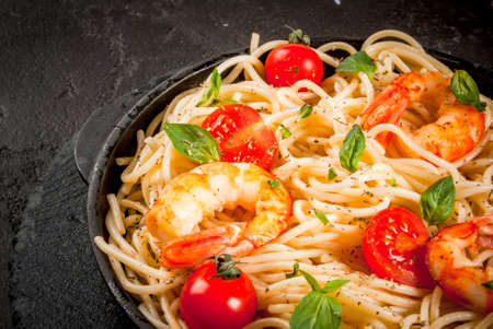 Seafood. Shellfish. Pasta with grilled prawns shrimps, with tomatoes, fresh herbs (basil) and spices. On a black cast-iron frying pan on a black concrete table, Close view, copy spaceの写真素材