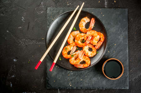 Seafood. Shellfish. Fried grilled shrimp prawns on wooden skewers, with soy sauce, asian style. Snack, appetizer. On black concrete table, copy space top viewの写真素材