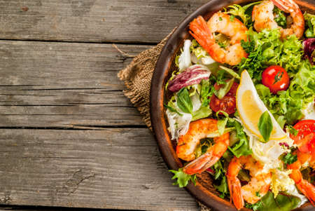 Seafood. Shellfish. Fresh lettuce salad with tomatoes, herbs and grilled fried shrimps prawns, on wooden rustic table, copy space top close viewの写真素材