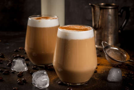 Morning. Breakfast. Classic summer cold coffee latte with whipped milk, ice and cinnamon. On  black background. Milk, coffee pot, strainer for strewing. Copy spaceの写真素材