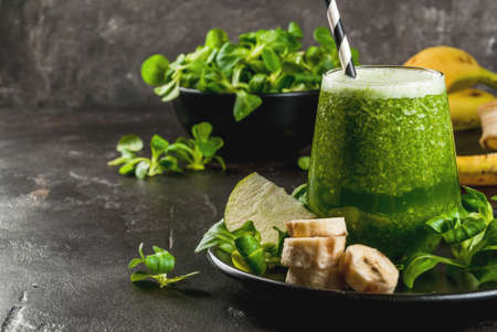 Organic vegetarian food. Fresh homemade raw vegetable and fruit green smoothie with apple, banana and lettuce leaves. On black plate with ingredients, horizontal with copy spaceの写真素材