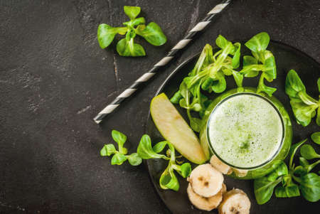 Organic vegetarian food. Fresh homemade raw vegetable and fruit green smoothie with apple, banana and lettuce leaves. On black plate with ingredients. top view with copy spaceの写真素材