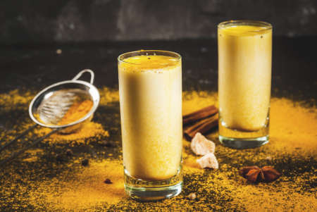 Traditional Indian drink turmeric milk is golden milk with cinnamon, cloves, pepper and turmeric. On a concrete table, with spices on the background. In glasses, Horizontal, tonedの写真素材