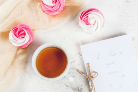 The concept of celebrating the mother's day. Spring relax. Cakes in the form of flowers (roses), with a cup of freshly brewed black tea, on a white stone table. With a blank note (copy space) top viewの写真素材