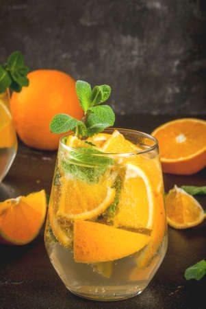 Summer refreshing orange drink. Detox, diet, infused. Variations on lemonade. Mineral water with pieces of fresh orange and mint. On a black stone concrete table, copy space toned verticalの写真素材