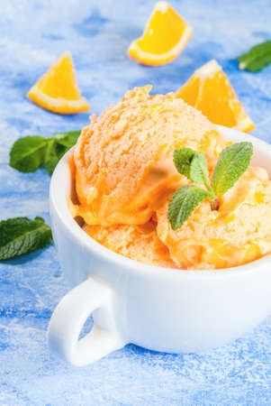 Homemade organic orange sorbet with orange slices and mint leaves. On a blue stone table, vertical, copy spaceの写真素材
