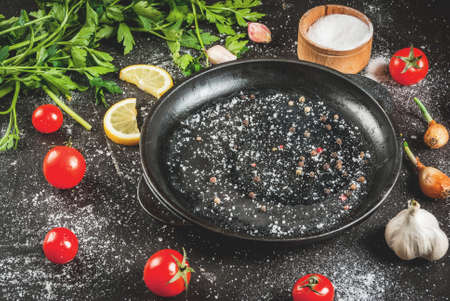 Cooking, background. Ingredients and spices for cooking dinner: tomatoes, greens (parsley), salt, pepper, onions, shallots, garlic. With a frying pan, on a black concrete table, copy spaceの写真素材