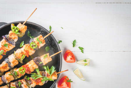Fajita chicken kebabs, with chicken meat, pepper, chili, tomatoes, onions, lime juice and herbs. In a frying pan, on a white wooden table. Mexican cuisine, a traditional food, Top close view, copy spaceの写真素材