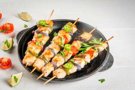 Fajita chicken kebabs, with chicken meat, pepper, chili, tomatoes, onions, lime juice and herbs. In a frying pan, on a white wooden table. Mexican cuisine, a traditional food, Close view, copy spaceの写真素材