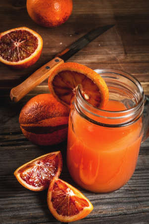 Refreshing summer drink. Juice from red Sicilian oranges. On a rustic wooden table, with whole and cut oranges. Copy spaceの写真素材