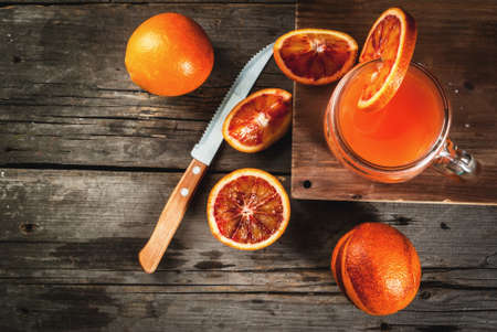 Refreshing summer drink. Juice from red Sicilian oranges. On a rustic wooden table, with whole and cut oranges. Copy spaceの写真素材
