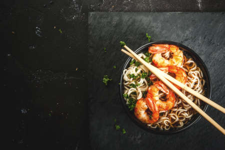 Asian soup with noodles (ramen), with miso paste, soy sauce, greens and shrimps prawn. On a black stone table, with chopsticks. Copy space top viewの写真素材