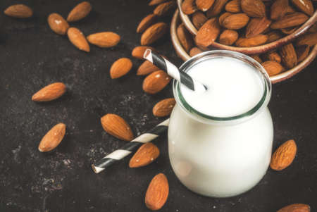 Vegetable sources of protein. Vegan healthy food. A small bottle of almond milk, portion. Against the backdrop of nuts, almonds, on a black concrete table. Selective focus. Copy spaceの写真素材