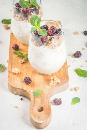 Dietary vegan healthy breakfast. Yogurt and granola with fresh  blueberry oranges and mint in a glass. On a white table, on a cutting board. Copy spaceの写真素材