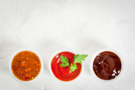 Three kinds of red tomato sauce on a white stone table: traditional classic ketchup, barbecue sauce, sweet and sour Chinese sauce. Top view copy spaceの写真素材