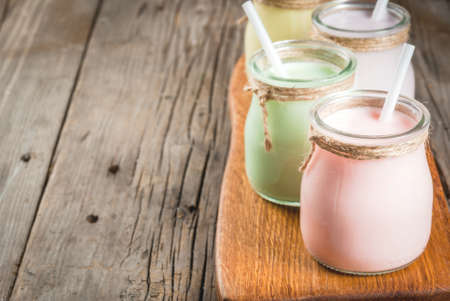 Small jars with a multi-colored smoothie or milkshake - pink cherry, purple berry, green and yellow orange. On a rustic wooden table copy spaceの写真素材