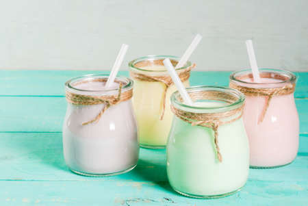 Small jars with a multi-colored smoothie or milkshake - pink cherry, purple berry, green and yellow orange. On a light blue wooden table copy spaceの写真素材