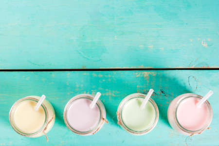 Small jars with a multi-colored smoothie or milkshake - pink cherry, purple berry, green and yellow orange. On a light blue wooden table copy space top viewの写真素材