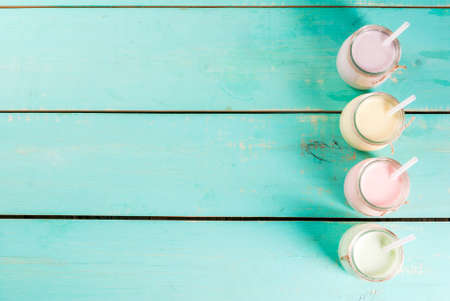 Small jars with a multi-colored smoothie or milkshake - pink cherry, purple berry, green and yellow orange. On a light blue wooden table copy space top viewの写真素材