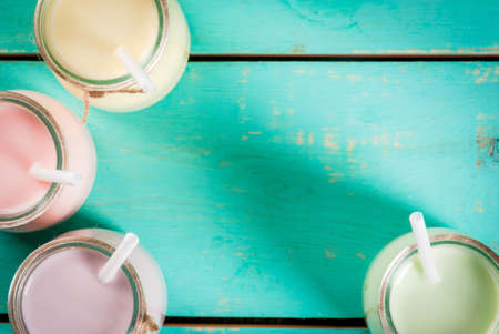 Small jars with a multi-colored smoothie or milkshake - pink cherry, purple berry, green and yellow orange. On a light blue wooden table copy space top close viewの写真素材