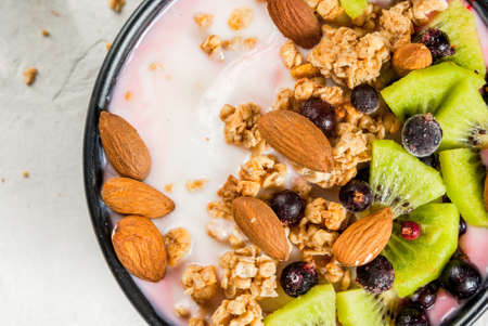 Healthy diet breakfast: smoothies bowl, with yogurt, fresh blueberries (black currant), kiwi, granola oatmeal, almond nuts. On a white stone table, with a glass of water and ingredients. Close viewの写真素材