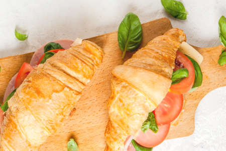 Light and hearty spring breakfast. Croissant with ham, cheese, fresh tomatoes and basil. On a white stone table, with the ingredients. Copy space top viewの写真素材