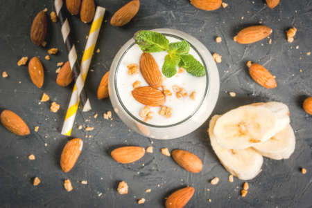 Healthy food. Dietary breakfast or snack. White smoothies made from yogurt, banana and almond nuts. decorated with mint. On a dark concrete table with ingredients, striped straws. Top viewの写真素材