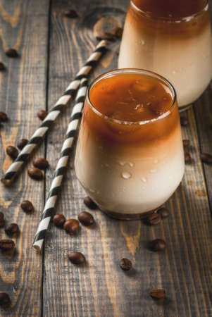 Cold coffee with milk, caramel and ice, with cubes of frozen coffee. Cappuccino, frapuchchino or latte. On awooden dark table, with coffee beans and striped straws. Copy space top viewの写真素材