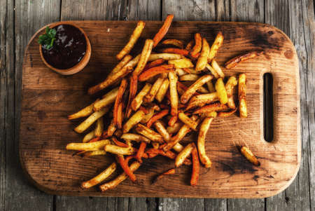 Homemade food. Fried French potatoes and carrots, on a serving board, with barbecue sauce on a rustic wooden table. Top viewの写真素材
