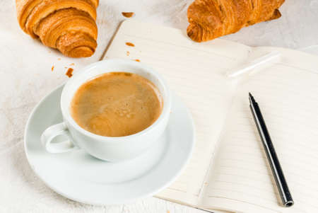 Relaxation. Job. Planning of affairs. White stone table with a notebook for notes, cases, tasks. A cup of fragrant freshly brewed coffee. Freshly baked croissants. Pencil. Copy spaceの写真素材