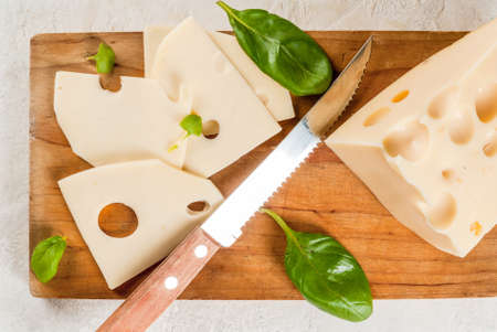 Maasdam radomer cheese on a cutting board, with leaves of basil. On a white stone concrete table. Copy space top viewの写真素材