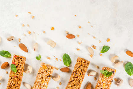 Healthy snack. Fitness. Dietary food. Four cereal granola bars with nuts and fruit berries, with ingredients on a white stone table. Top view copy spaceの写真素材