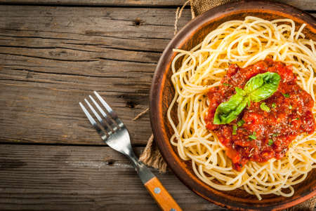 Italian cuisine. Lunch or dinner. A serving of spaghetti pasta with tomato marinara sauce and basil on a dark wooden table. Copy space top viewの写真素材