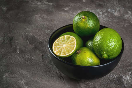 Fresh organic tropical citrus fruits lime in a black bowl on a gray concrete background. Whole and half. Copy spaceの写真素材
