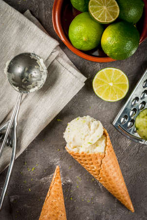 Refreshing lime sorbet in a bowl with a spoon for ice cream. With horns for ice cream (one full of ice cream), limes, grater for peel. On an old gray concrete table. Copy space top viewの写真素材