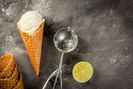 Homemade lemon ice cream. Horn with sorbet, sprinkled with zest, spoon and half lime. On a gray concrete old table. Top view copy spaceの写真素材