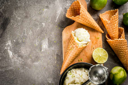 Refreshing lime sorbet in a bowl with a spoon for ice cream. With horns for ice cream (one full of ice cream), limes, grater for peel. On an old gray concrete table. Top view copy spaceの写真素材