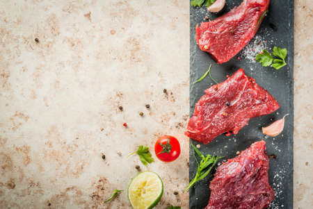 Fresh raw beef meat tenderloin steaks on a slate cutting board on a light beige stone table. With...