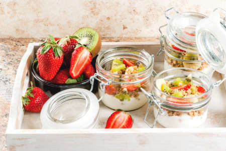 Healthy breakfast. Diet. Overnight oatmeal in a can, muesli. Yogurt with homemade granola and organic fruits - kiwi, banana, strawberry. On the stone table.  Copy spaceの写真素材