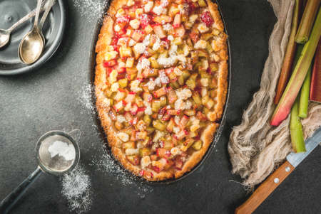 Bakery. Ready freshly baked homemade pie with rhubarb and sugar. Shortbread. Rustic style. On a stone black table. With sugar powder for sprinkling. Top view,  copy spaceの写真素材