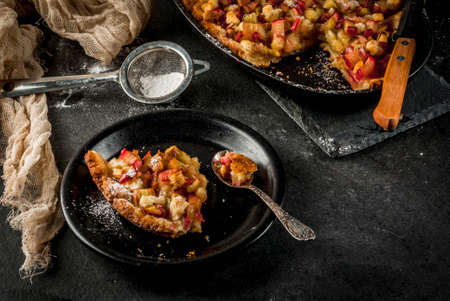 Bakery. Ready freshly baked homemade pie with rhubarb and sugar. Shortbread. Rustic style. On a stone black table. Sugar powder for sprinkling. One piece on a plate. Copy spaceの写真素材