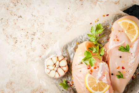 Fresh raw unprepared chicken fillet, breast. With spices, herbs, garlic and lemon for cooking. On a light stone table. Copy spaceの写真素材