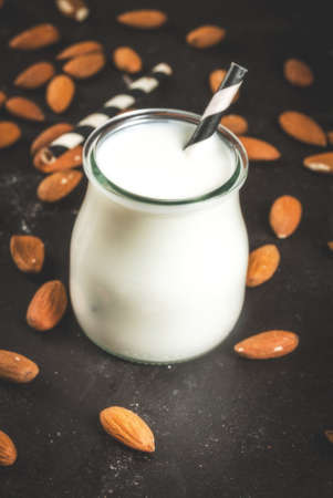 Vegetable sources of protein. Vegan healthy food. A small bottle of almond milk, portion. Against the backdrop of nuts, almonds, on a black concrete table. Selective focus. Copy spaceの写真素材