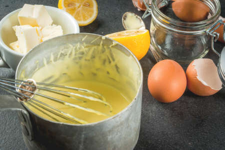Traditional basic sauces. French cuisine. Hollandaise sauce in a metal saucepan, with ingredients for cooking - eggs, butter, lemons. On a black stone table. Copy space top viewの写真素材