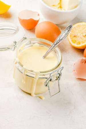 Traditional basic sauces. French cuisine. Hollandaise sauce in glass jar, with ingredients for cooking - eggs, butter, lemons. On a white concrete stone table. Copy spaceの写真素材
