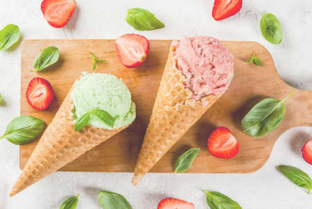 Summer fresh desserts. Green basil and red strawberry ice cream in a cone. On a white stone table with basil leaves and fresh strawberries around. On a white stone table.の写真素材