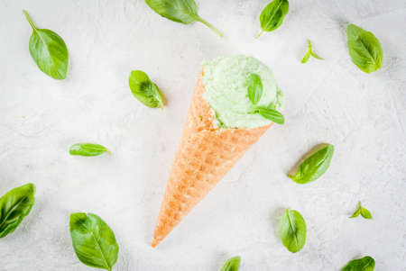 Summer fresh desserts. Green basil ice cream in a cone. On a white stone table with basil leaves around.の写真素材