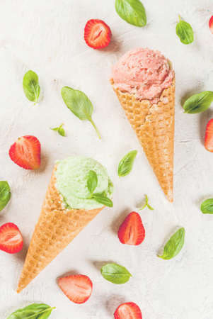 Summer fresh desserts. Green basil and red strawberry ice cream in a cone. On a white stone table with basil leaves and fresh strawberries around. On a white stone table.の写真素材